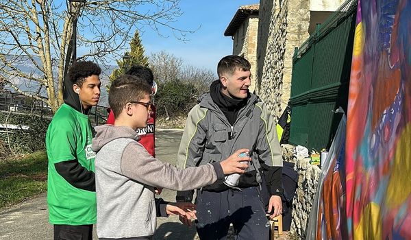 Tres niños con discapacidad pintando con pintura de spray una tela en la calle.