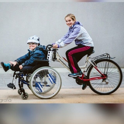 Niña llevando a bici a un niño con discapacidad en silla de ruedas.