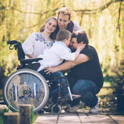 Familia feliz abrazándose con un niño con discapacidad en silla de ruedas.
