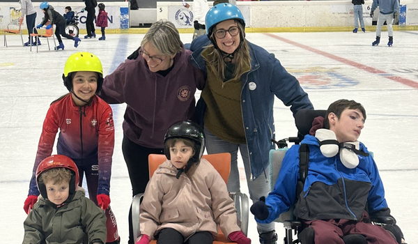 Dos chicas adultas con 4 niños, dos de ellos con discapacidad, patinando sobre hielo.