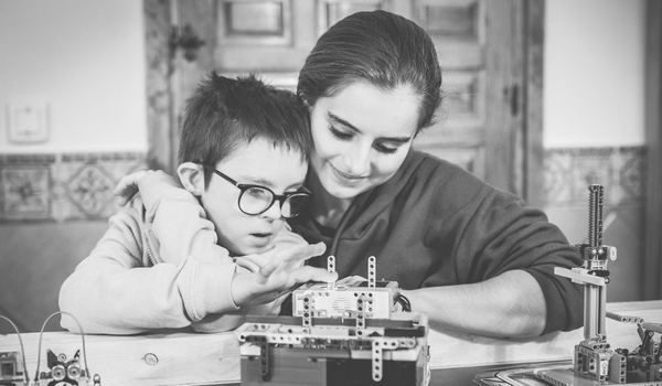 Niño con discapacidad montando legos de robótica acompañado de una mujer adulta.